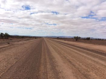 Dirt road amidst field against sky