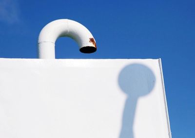 Close-up of boat air pipe and flagpole shadow against blue sky 