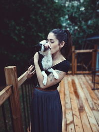 Woman kissing dog while standing outdoors