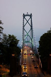 Vehicles on suspension bridge against sky in city