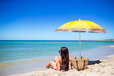 Rear view of woman with umbrella at beach against clear blue sky