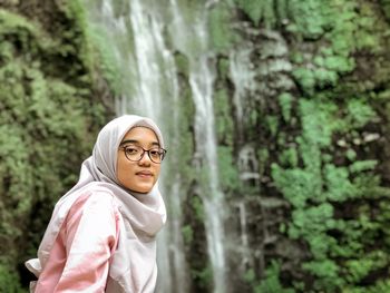 Portrait of young woman against waterfall and trees in forest