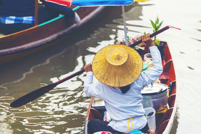 Rear view of man wearing hat rowing boat on river