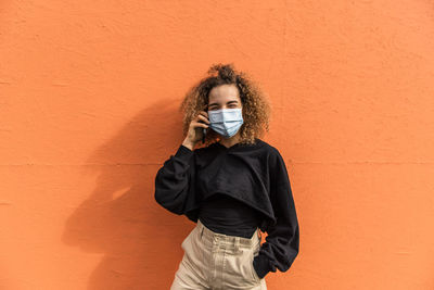 Portrait of young woman standing against orange wall