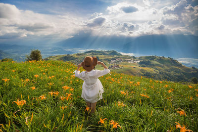 Rear view of woman standing amidst flowering plants against sky