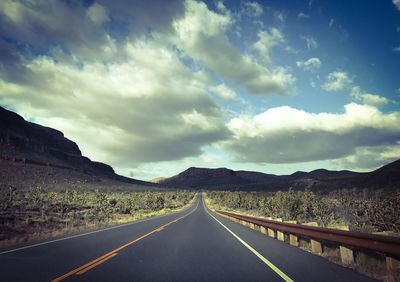 Empty road by mountains against sky