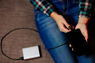 Midsection of woman charging mobile phone with portable charger