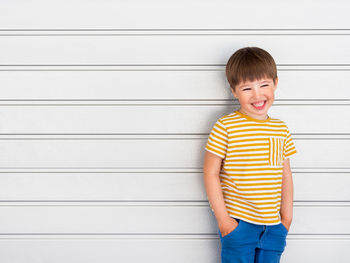 Portrait of smiling boy on white background. cute kid stands hands in pockets near light grey wall.