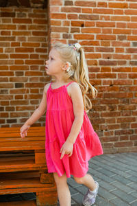 Full length of cute girl standing against brick wall