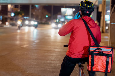 Rear view of man with bicycle on street at night