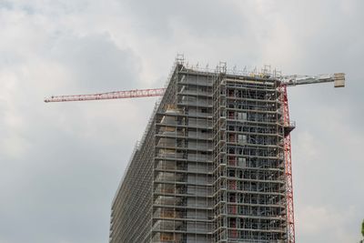 Low angle view of crane by building against sky