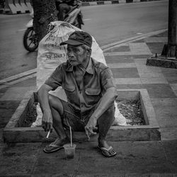 Full length of man sitting on footpath