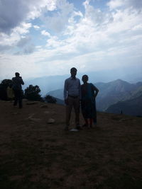 Rear view of people standing on mountain against sky