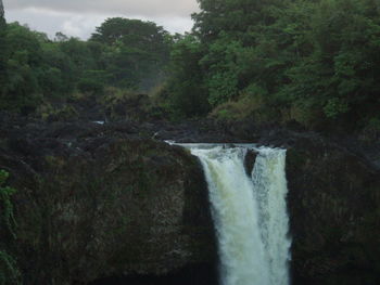 Scenic view of waterfall in forest against sky