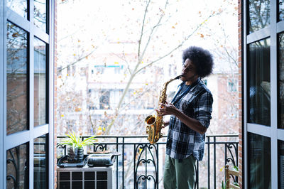 Afro male musician practicing saxophone in balcony at home