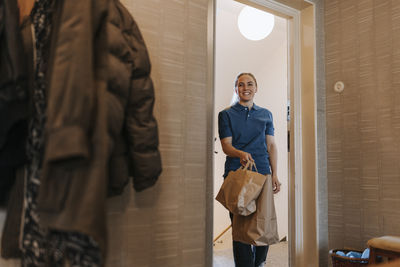 Smiling female healthcare worker entering in house through doorway