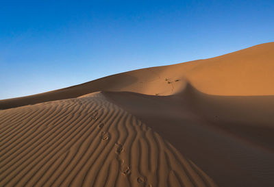 Low angle view of sand dunes against clear blue sky