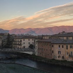 Buildings by river against sky during sunset