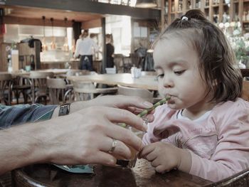 Close-up of man hands helping girl to drink juice from glass on table in restaurant