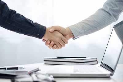 Cropped hands of colleagues handshaking by laptop on office desk