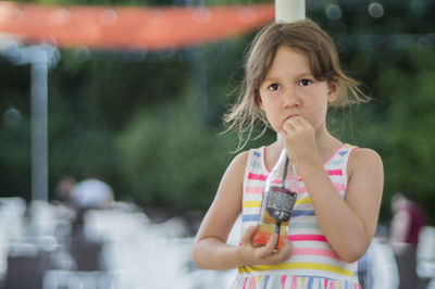 Girl drinking cold drink from bottle while standing at outdoor cafe