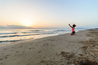 Side view of teenage girl jumping at beach during sunset