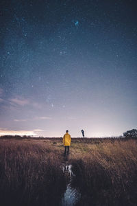 Rear view of man standing on field against sky at night