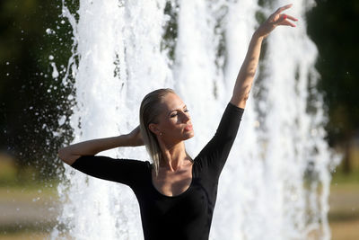 Young woman with arms raised standing against waterfall