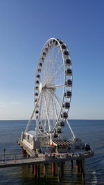 Ferris wheel by sea against clear blue sky