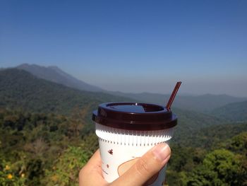 Midsection of person holding drink against mountain range