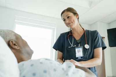 Low angle view of nurse looking at senior patient in hospital ward