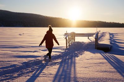 Full length of woman at frozen lake during sunset
