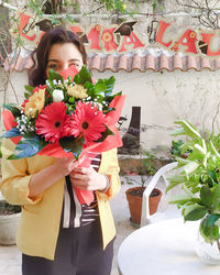 Woman holding flower bouquet against wall