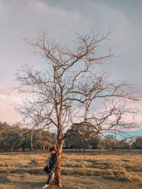 Man standing by bare tree on land against sky