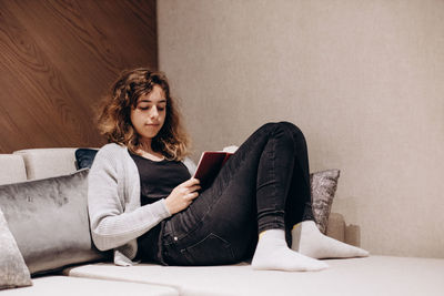 Teenager girl reading book on couch at home