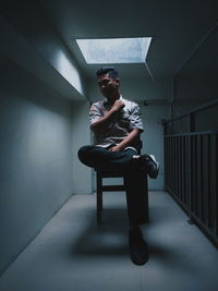 Young woman looking away while sitting on seat against wall