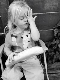 Irritated cute girl holding bread while sitting on chair in yard