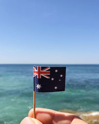 Person holding flag against sea against clear sky