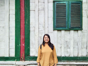 Portrait of smiling woman standing against wall