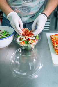 Unrecognizable cook in restaurant kitchen preparing salad to takeaway