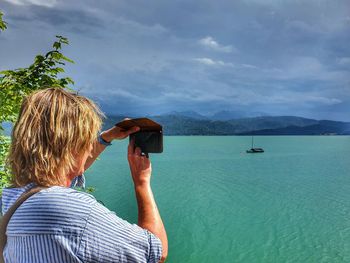 Rear view of woman photographing sea against sky