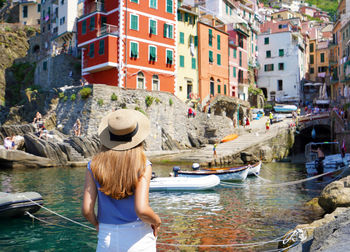 Pretty young woman looking at the village of riomaggiore from the harbor, cinque terre, italy.