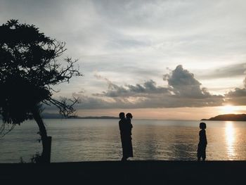 Silhouette men on beach against sky during sunset