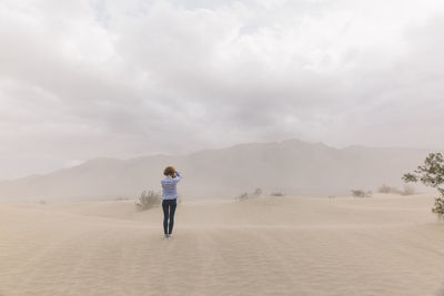 Rear view of woman standing on desert against sky