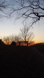 Silhouette bare trees on field against sky at sunset