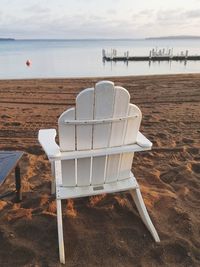 Deck chair on sand at beach against sky