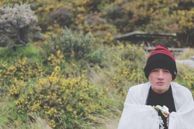 Portrait of young man shivering against plants at park