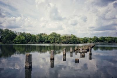 Wooden posts in lake against sky