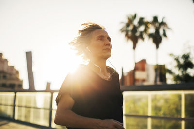 Thoughtful woman looking away while listening music at bridge during sunset