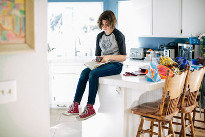 Teen girl sits on kitchen counter and places her bookmark in her book